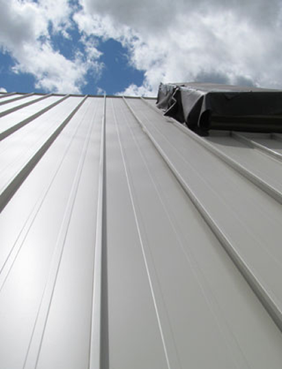 Standing seam metal roofing panels with clean lines and a clear blue sky background, showcasing durability and structural integrity for construction projects.