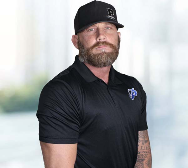 Chance Roberts, Co-Founder and President of Practical Building Systems, wearing a black polo shirt with logo and cap, posed against a blurred background.