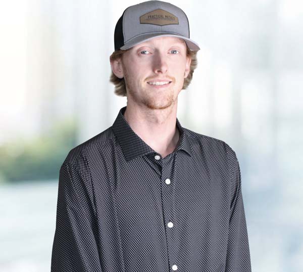 Man wearing a black polka-dot shirt and a Practical Metals cap, smiling in a professional setting, representing the Practical Metals team.